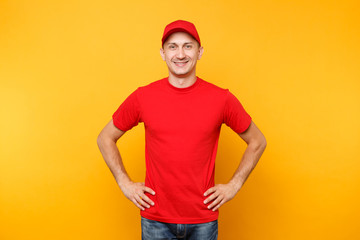 Delivery man in red uniform isolated on yellow orange background. Professional smiling male employee in cap, t-shirt working as courier or dealer standing with arms akimbo. Service concept. Copy space