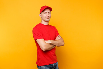 Delivery man in red uniform isolated on yellow orange background. Professional calm confident male employee in cap, t-shirt courier or dealer holding hands crossed folded. Service concept. Copy space.