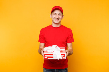 Delivery man in red uniform isolated on yellow orange background. Professional smiling male employee in cap, t-shirt working as courier or dealer holding red present box. Service concept. Copy space.