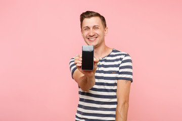 Portrait of man in striped t-shirt showing mobile phone camera with blank black empty screen copy space isolated on trending pastel pink background. People sincere emotions concept. Advertising area.