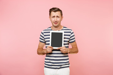 Portrait of young man holding tablet computer with blank black empty screen display touchscreen copy space isolated on trending pastel pink background. Technology lifestyle concept. Advertising area.