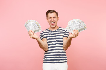 Portrait of happy excited young man in striped t-shirt holding bundle lots of dollars, cash money,...