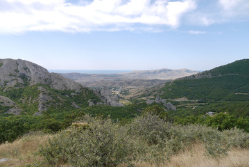 A landscape of mountainous terrain with mountain peaks and valleys covered with green forest and completely bare without a single tree.