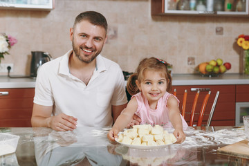 Little kid girl help man to cook lazy dumplings in light kitchen at table. Happy family dad, child daughter cooking food in weekend morning at home. Father's day holiday. Parenthood childhood concept.