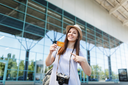 Young smiling traveler tourist woman with retro vintage photo camera, pointing index finger on credit card at international airport. Passenger traveling abroad on weekends getaway. Air flight concept.