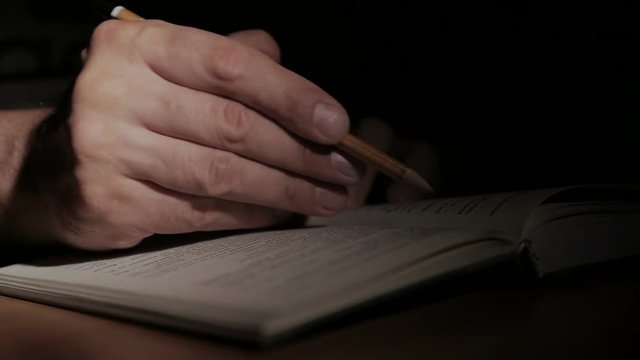 Close-up of a man's hand with an open paper book, writes a note with a pencil on the page