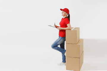 Full length of delivery woman in red cap, t-shirt isolated on white background. Female courier holding clipboard with papers document, blank empty sheet on empty cardboard boxes. Receiving package.