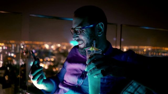 Young, happy man taking photo with cellphone on terrace by night, 4K
