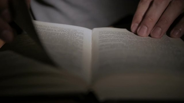 Close-up of a man's hand holding an open paper book, turning the pages with his fingers