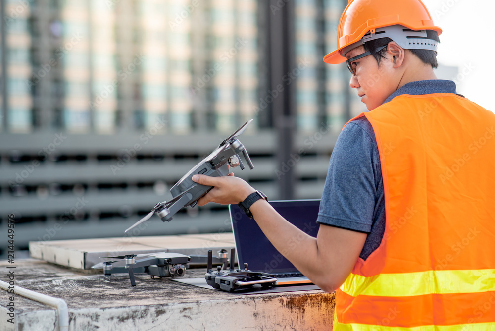 Wall mural young asian engineer man working with drone laptop and smartphone at construction site. using unmann