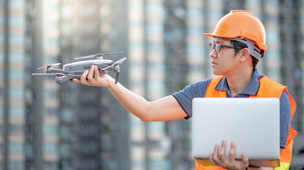 Young Asian man working with drone and laptop computer at construction site. Using unmanned aerial...