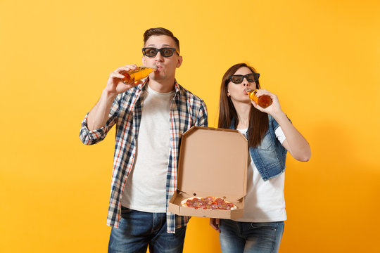 Young couple woman and man sport fan in 3d glasses cheer up support team holding italian pizza in cardboard flatbox drinking beer isolated on yellow background. Sport family leisure lifestyle concept.