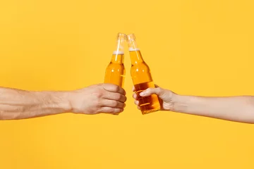 Foto op Aluminium Close up cropped of woman and man two hands horizontal holding lager beer glass bottles and clinking isolated on yellow background. Sport fans cheer up. Friends leisure lifestyle concept. Copy space. © ViDi Studio