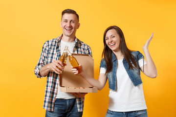 Young joyful couple woman man sport fan cheer up support team clinking beer bottles hold italian pizza in cardboard flatbox spread hands isolated on yellow background. Sport family leisure lifestyle.