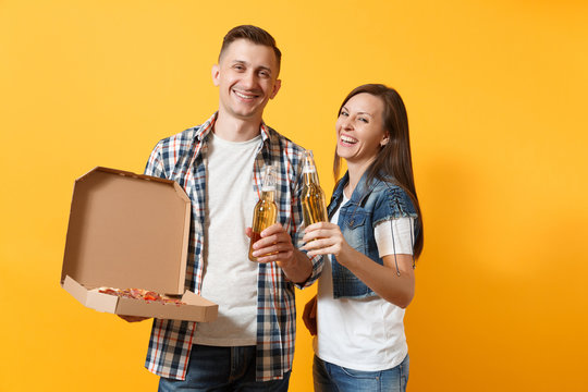 Young happy smiling couple woman and man sport fan cheer up support team hold beer bottles and italian pizza in cardboard flatbox isolated on yellow background. Sport family leisure lifestyle concept.