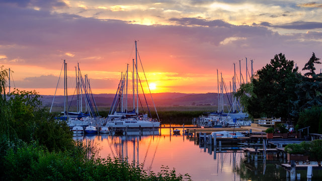 Stimmungsvoller Sonnenuntergang auf dem Neusiedlersee mit Blick auf das Leithagebirge im Vordergrund ein Segelyachthafen 