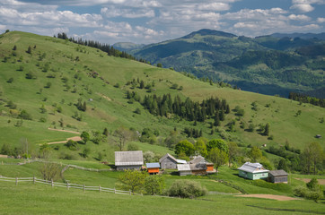 Fototapeta na wymiar Scenic shot of rural area at mountains taken at sunny spring day. Remote houses are scattered on the slope of the hill covered with forest and meadows. Concept of clear environment. Natural background