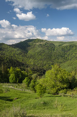 Scenic view of mountains taken at sunny spring day.  Hills covered with forest and meadows. Blue sky and clouds. Natural background. Ecology concept of clear environment.