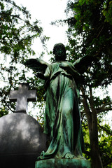 A weathered sandstone sculpture of an angel under trees.