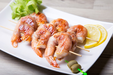 Shrimps grill in prosciutto with lemon and olives on a white plate. Close-up, selective focus.