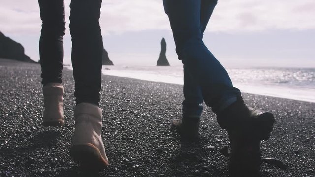 Close up shot of young couple holding hands running down black sand beach in Iceland, slow motion
