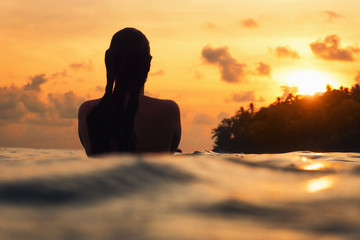 young woman from behind in indian ocean during orange sunset with romantic mood