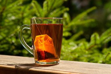 Tea and tea bag under the summer sun. A tea bag in a glass mug on the windowsill and against the background of green summer trees.