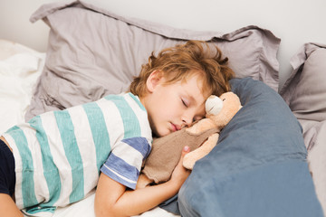 Little preschool kid boy sleeping in bed with a toy a bear.
