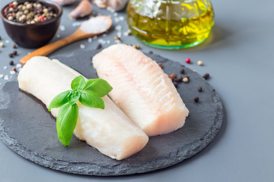 Fresh raw cod fillet with spices, pepper, salt, basil on stone plate, horizontal, copy space