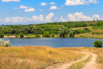 Fototapeta na wymiar Summer landscape with dirt road to the lake and blue sky with white clouds