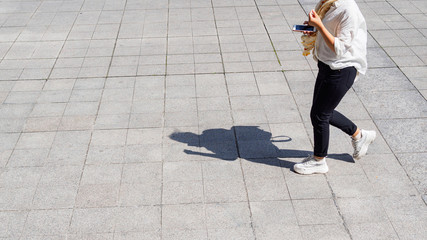 Woman walking and holding her mobile phone on pedestrian with black silhouette shadow on ground. 