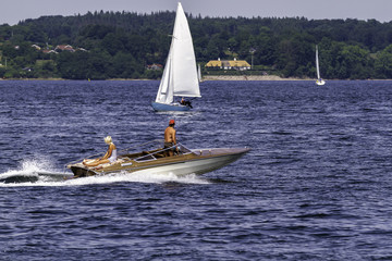 Obraz premium Paar mit Motorboot auf dem Meer unterwegs schaut auf Segelboote.