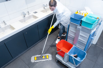 Cleaning lady mopping the floor in restroom cleaning the toilet 