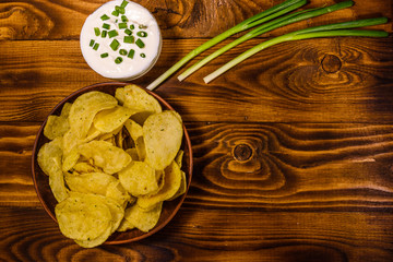 Ceramic plate with potato chips and glass bowl with sour cream on wooden table. Top view