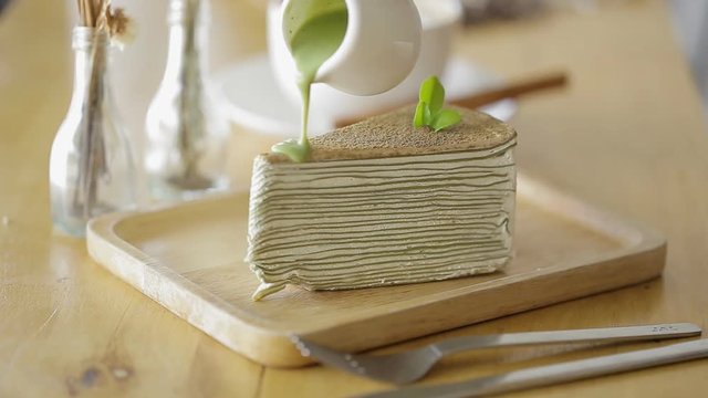 Cutting Green tea crepe cake with knife on wooden plate.