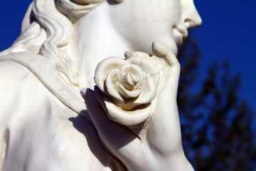 Head of white marble beautiful stone statue with rose in the hand close up on sky background