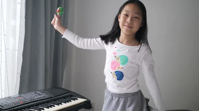 Asian girl playing maracas slow motion with gray background at home