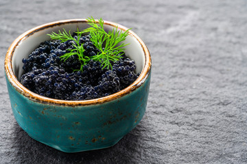 Black lumpfish caviar in a small pot on dark backgournd