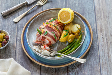 Bacon-wrapped haddock stuffed with crayfish tails, with lemony new potatoes, green beans and olives - high angle view