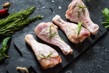 Photo sur Plexiglas Viande Cuisses de poulet crues non cuites, pilons sur planche de pierre, viande avec ingrédients pour la cuisson.