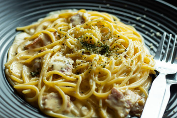 The spaghetti, fried cheese on a black plate on the table.