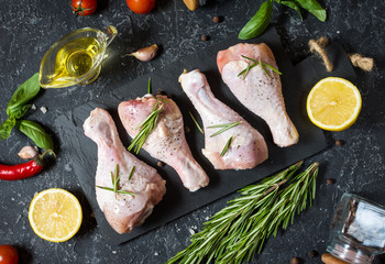 Raw uncooked chicken legs, drumsticks on stone board, meat with ingredients for cooking