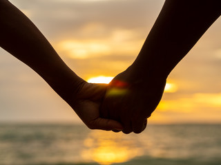 Couple holding hands on beautiful sunset background at the beach. Love & Family Concept.