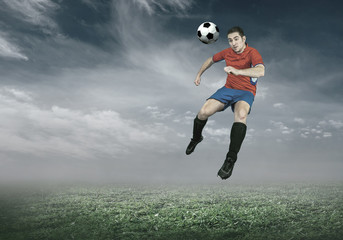 Fototapeta na wymiar Football player with ball in action under sky with clouds