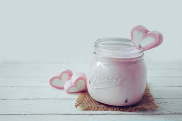 Pink milkshake with heart shape marshmallows on wood background