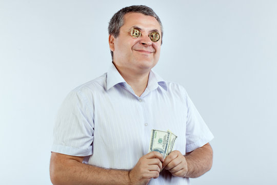 Businessman with bitcoins in his eyes smiles. He's holding dollars in his hands.
