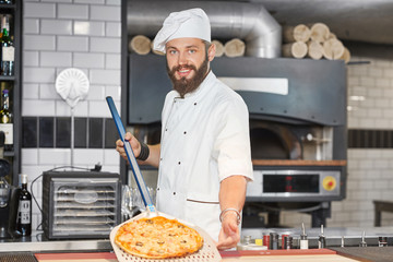 Front view of baker wearing chef's tunic and keeping pizza on metallic shovel.