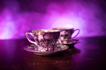 Food background tea and coffee theme. Old vintage ceramic tea or coffee pot with cups jug and sugar cup on dark background with lights and smoke. Silhouettes of ceramic tea pot and cup.