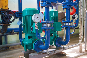Two green electric pump on a water pipeline painted in blue. Industrial background.