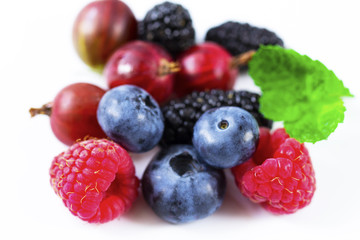 Close-up arrangement mixed, assorted berries including blackberries, strawberry, blueberry, raspberries and fresh leaf on white